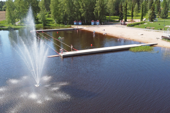 Kesäinen ilmakuva Rivieran rannalta, suihkulähde kohoaa korkealle ja ihmisiä on uimassa.